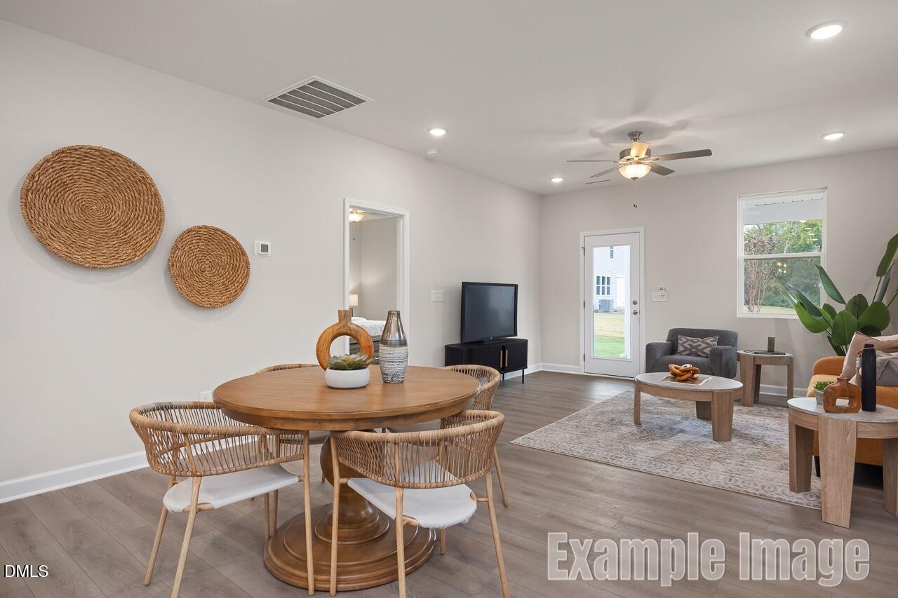 Open-concept living and dining area with round wooden table, wicker chairs, TV console, and neutral decor in The Carter C floor plan, Lillington, NC
