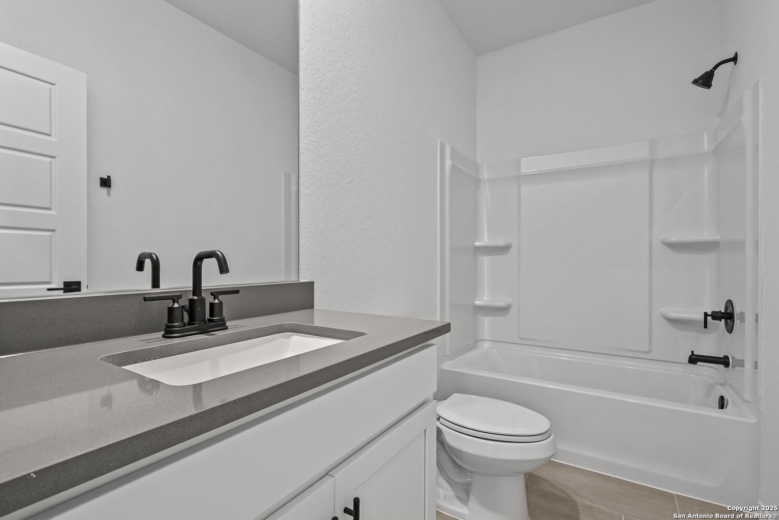 Contemporary bathroom with glass walk-in shower, soaking tub, gray quartz vanity, and black fixtures in Davidson Homes The Daphne J, Converse TX