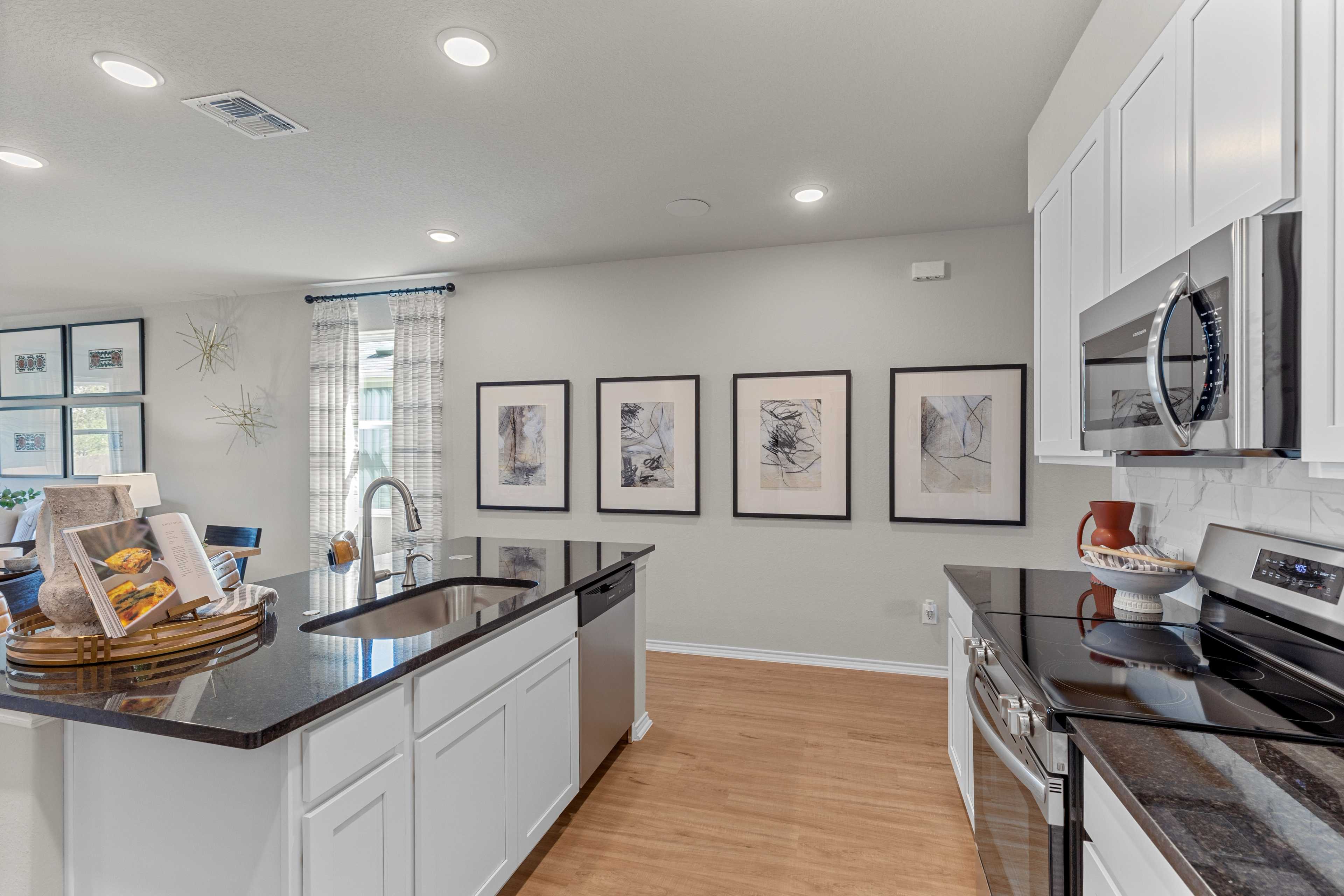 Modern kitchen in The Sabine C showcasing white shaker cabinets, black granite island with sink, stainless steel appliances, San Antonio home