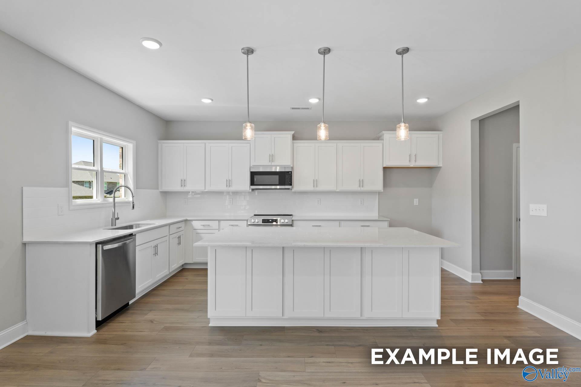 Modern white kitchen with island, quartz countertops, and pendant lighting in The Chelsea A at Walker's Hill, Meridianville.