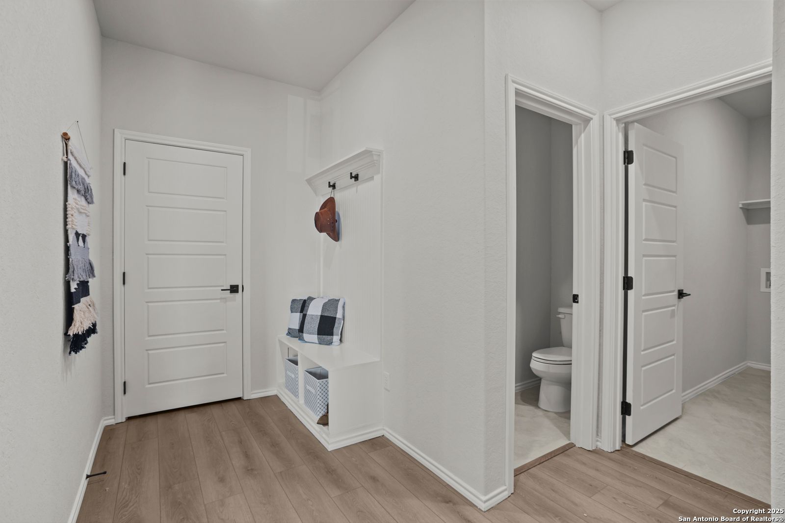 Bright entryway with built-in plaid bench, coat hooks, and adjacent powder room in Davidson Homes The Douglas C, Seguin, Texas