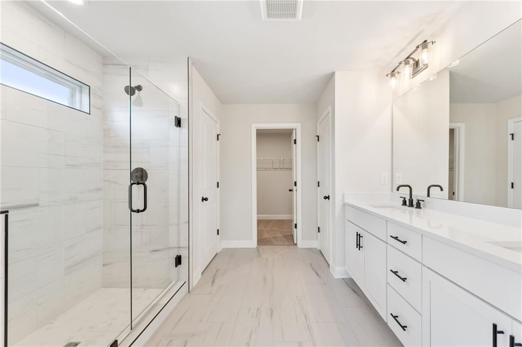 Modern master bathroom with frameless glass shower, double white vanity, and closet door in Davidson Homes The Hickory B, Buford, GA