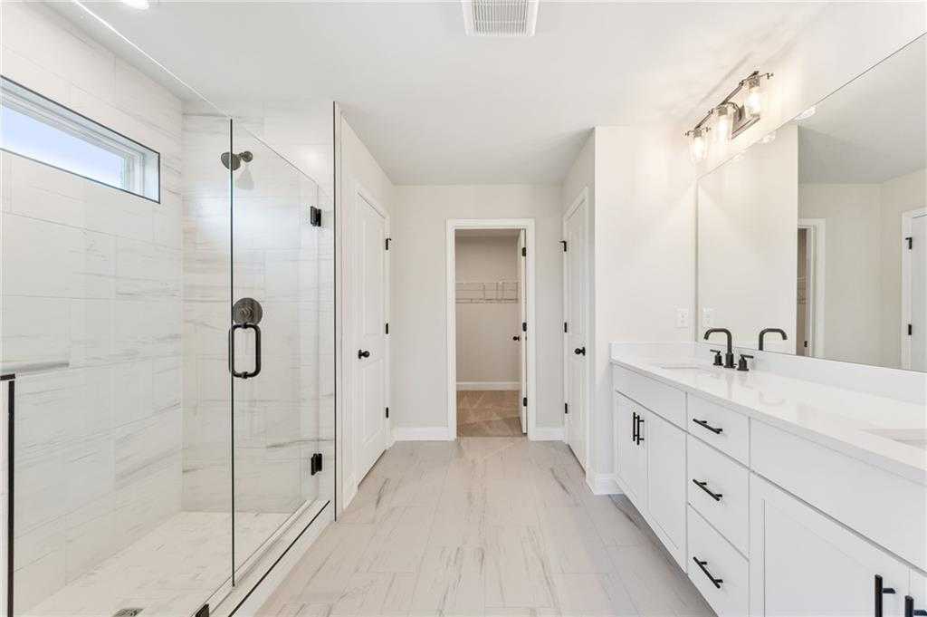 Modern master bathroom with frameless glass shower, double white vanity, and closet door in Davidson Homes The Hickory B, Buford, GA
