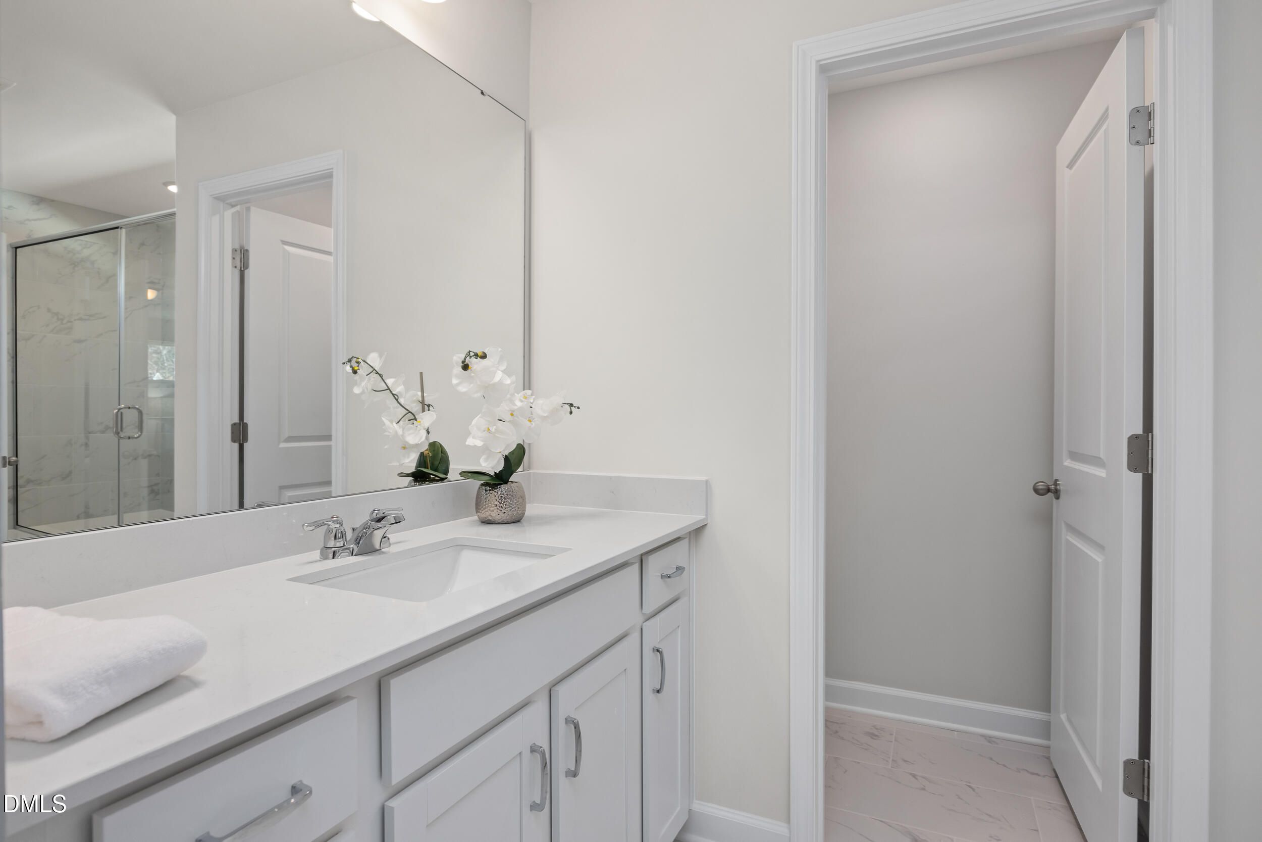 Elegant primary bathroom with white double vanity, large mirror, glass shower, and orchids in Davidson Homes The Preston C, Lillington, NC