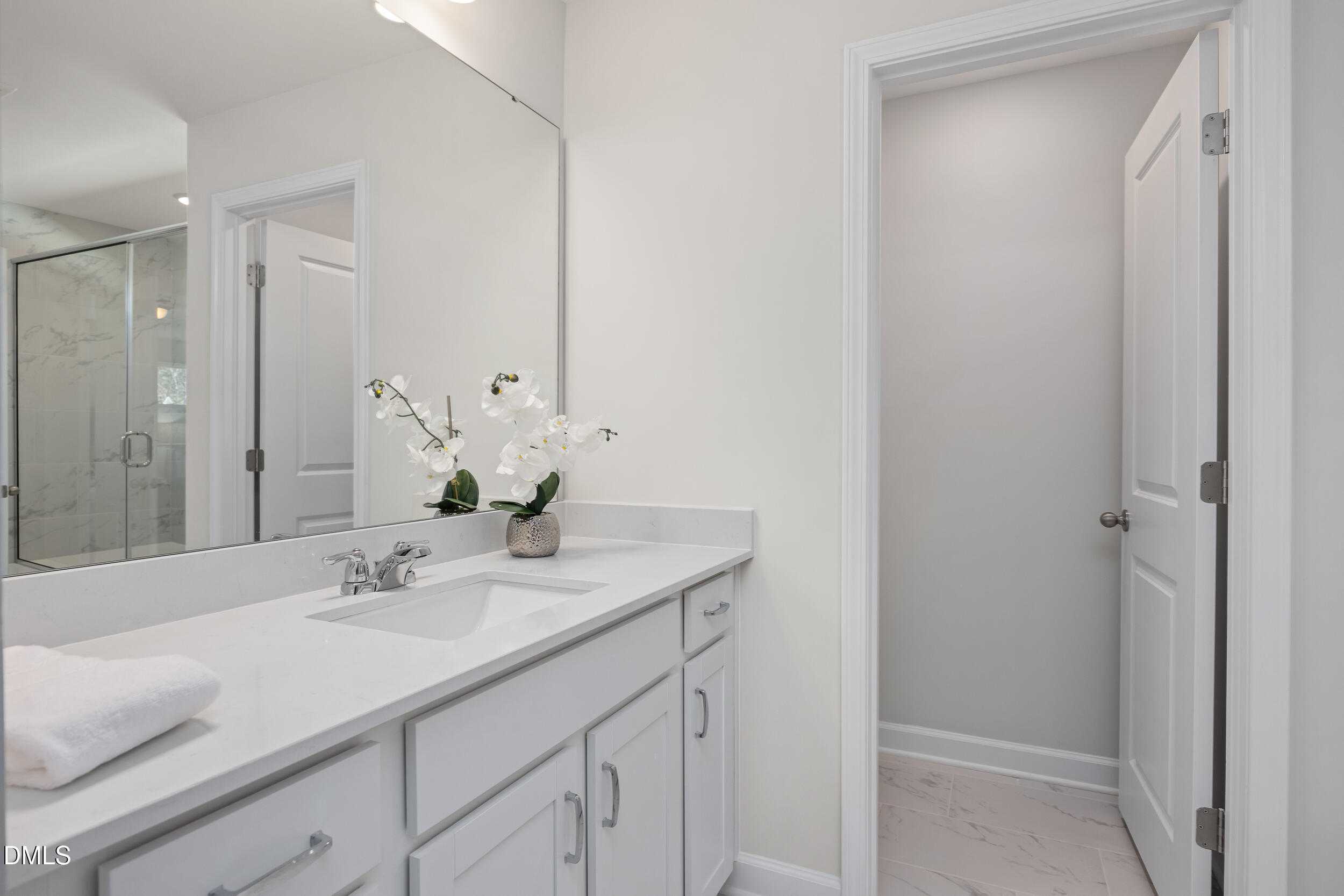 Elegant primary bathroom with white double vanity, large mirror, glass shower, and orchids in Davidson Homes The Preston C, Lillington, NC