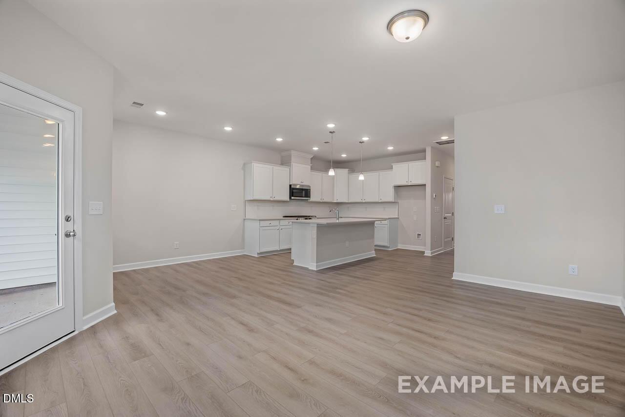 Modern open kitchen featuring white shaker cabinets, large island, stainless appliances, and hardwood floors in Davidson Homes The Graham, Fuquay-Varina, NC