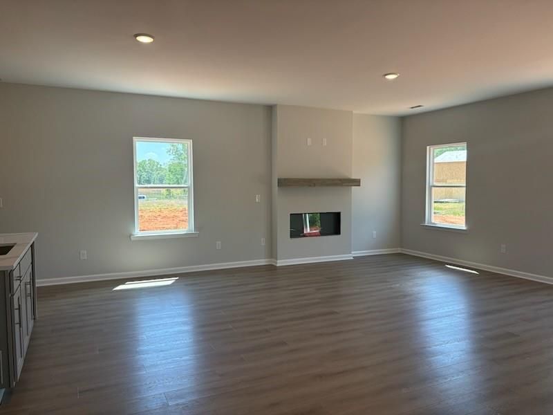 Spacious open living room with wood mantel fireplace, hardwood floors, and large windows overlooking greenery in Davidson Homes The Rabun A, Winder, Georgia