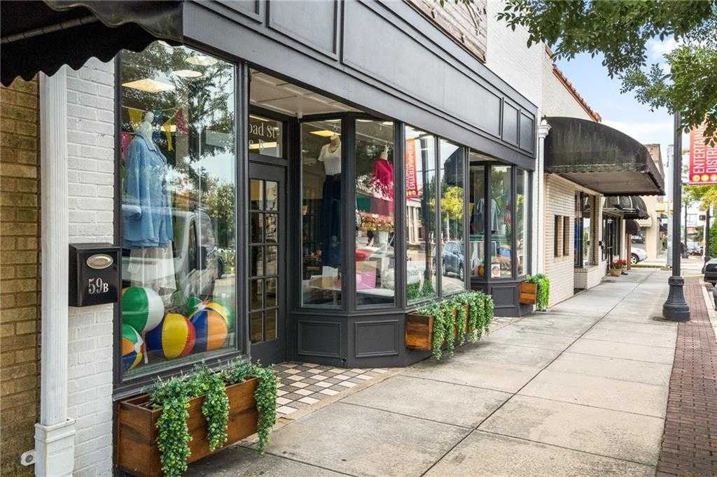 Charming boutique storefront with colorful clothing displays, potted plants, and brick facade on tree-lined sidewalk in Winder, Georgia