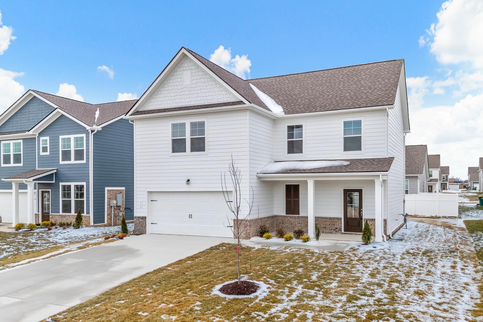 Two-story white Craftsman home with brown roof, covered porch, two-car garage, and snowy yard in Sage Farms, White House, Tennessee