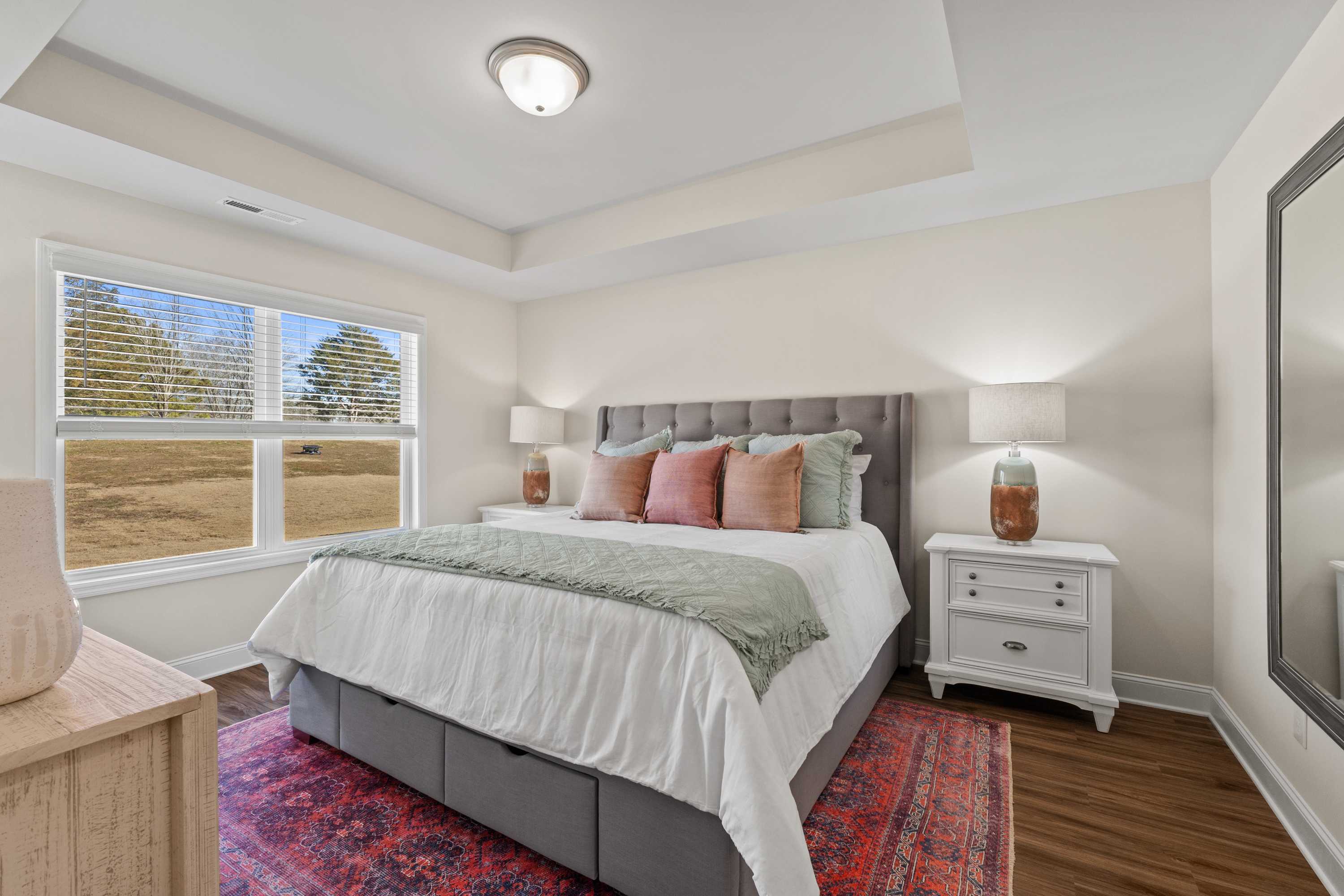 Spacious master bedroom at Berry Cove in New Market, Alabama with gray tufted bed, neutral walls, hardwood floors and scenic window
