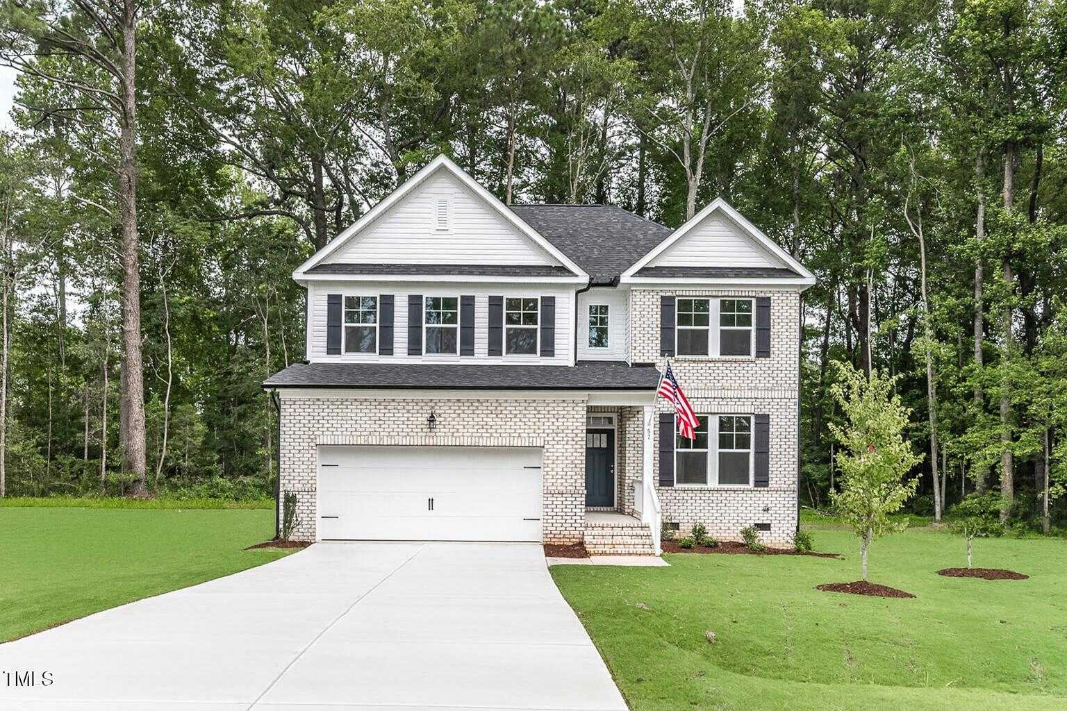 Two-story white brick Davidson Homes Willow C with 2-car garage, front porch, and American flag in Wellers Knoll, Lillington, NC
