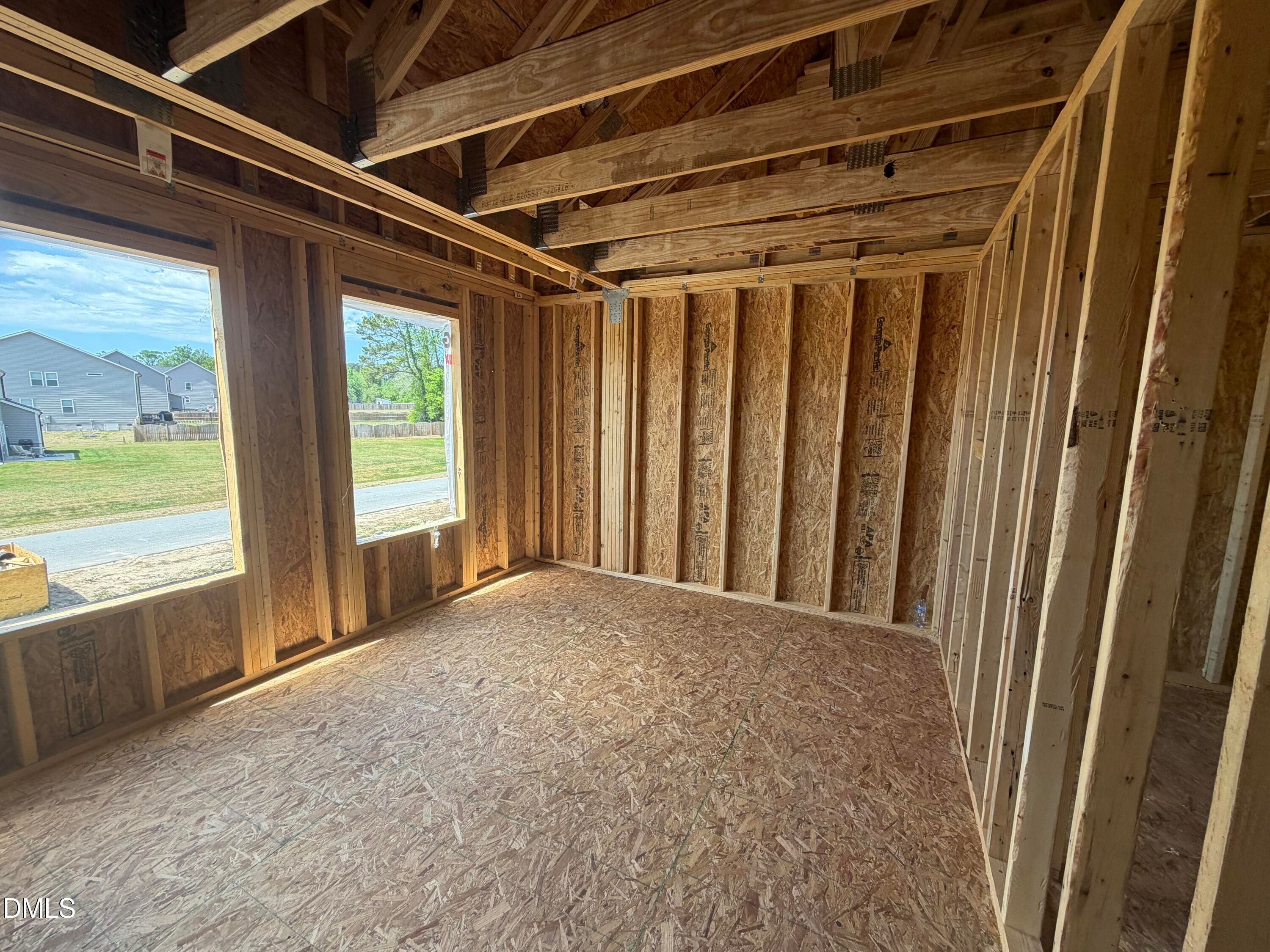 Framed living room with exposed wooden trusses, OSB walls, plywood floors, and large windows overlooking yard in Davidson Homes Hickory II C, Lillington NC