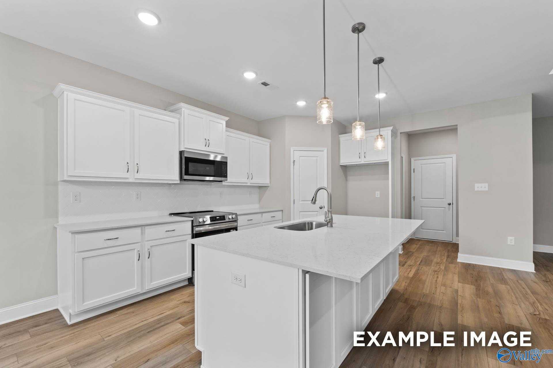 Modern white kitchen with large island, stainless appliances, pendant lights, and hardwood floors in Davidson Homes The Montgomery, Meridianville AL