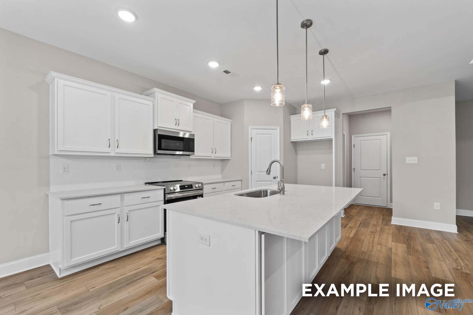 Modern white kitchen with large island, stainless appliances, pendant lights, and hardwood floors in Davidson Homes The Montgomery, Meridianville AL