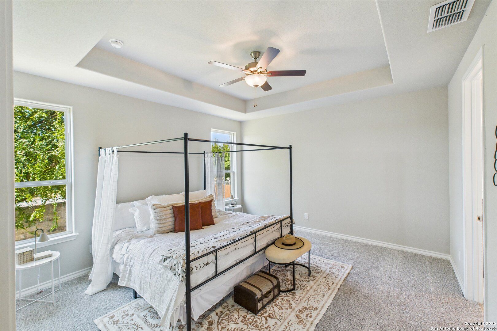 Elegant canopy bed with white linens and orange pillows in tray-ceiling bedroom, Davidson Homes The Jennings H, Ladera, San Antonio, Texas