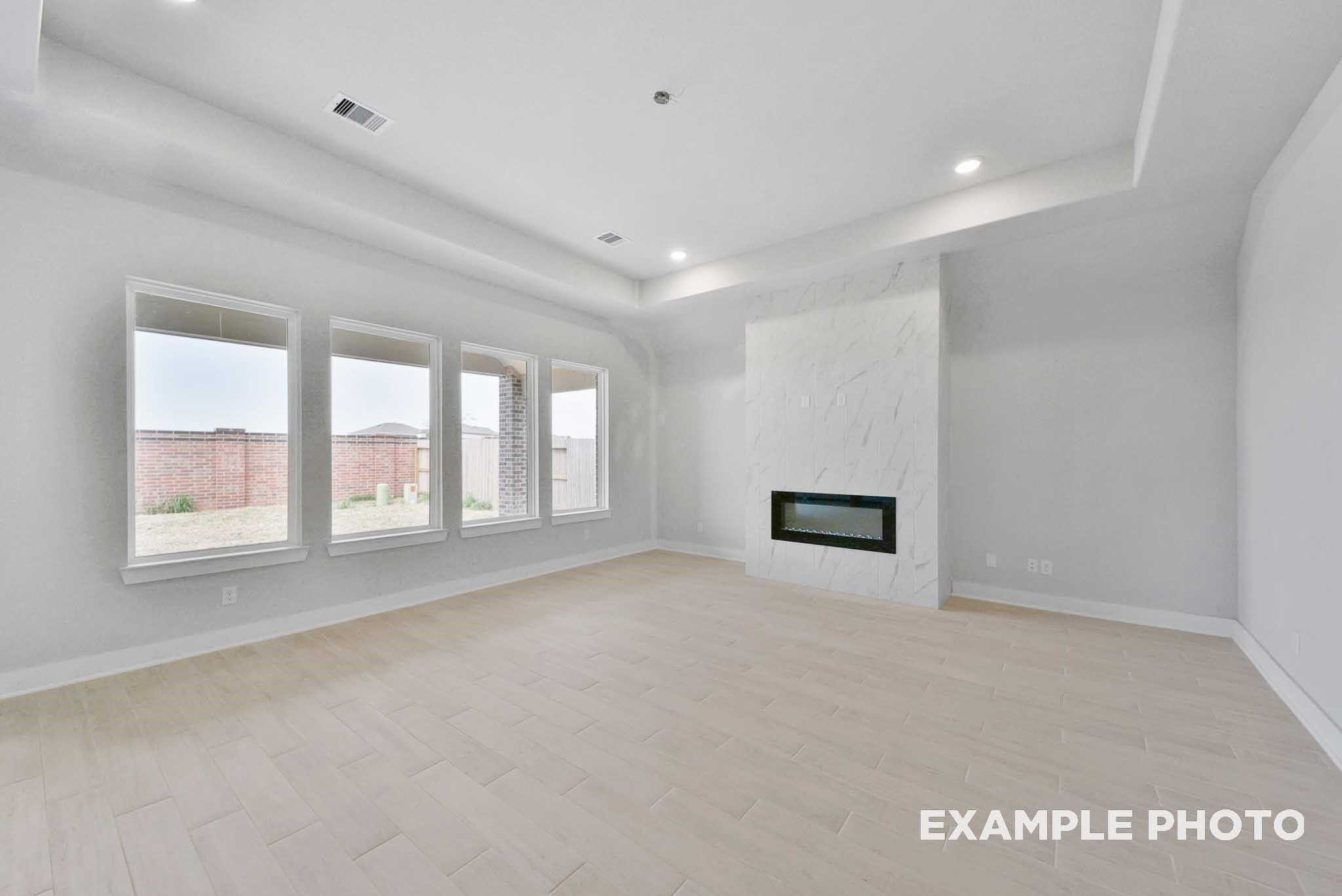 Spacious living room with modern white linear fireplace, large windows, and tray ceiling in Davidson Homes The George A, Lago Mar, Texas City