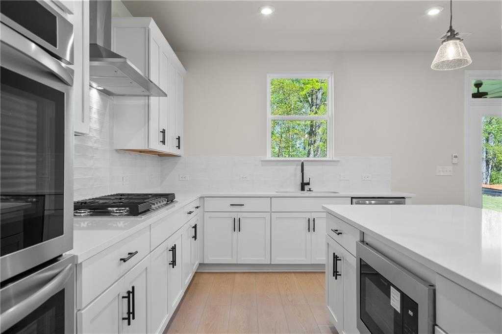 Bright white kitchen with shaker cabinets, stainless double ovens, gas range, quartz island in The Hickory B, Buford, GA