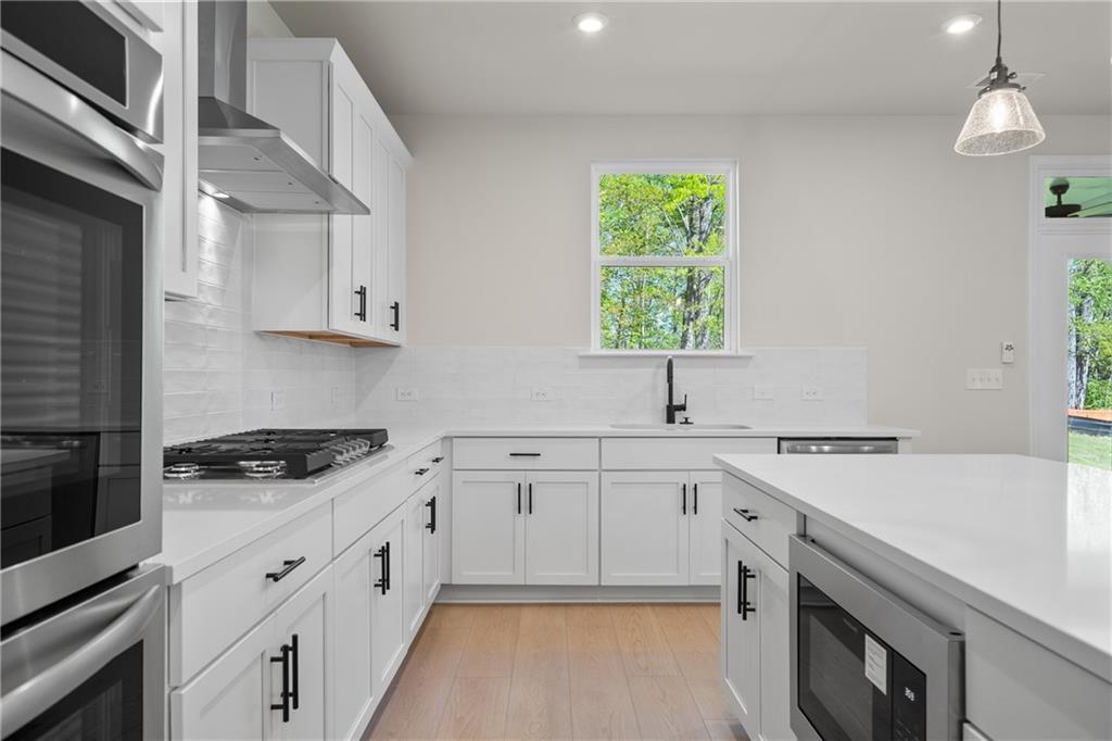 Modern white shaker kitchen with stainless steel appliances, quartz island, gas range, and tree-view window in The Hickory E, Buford, GA