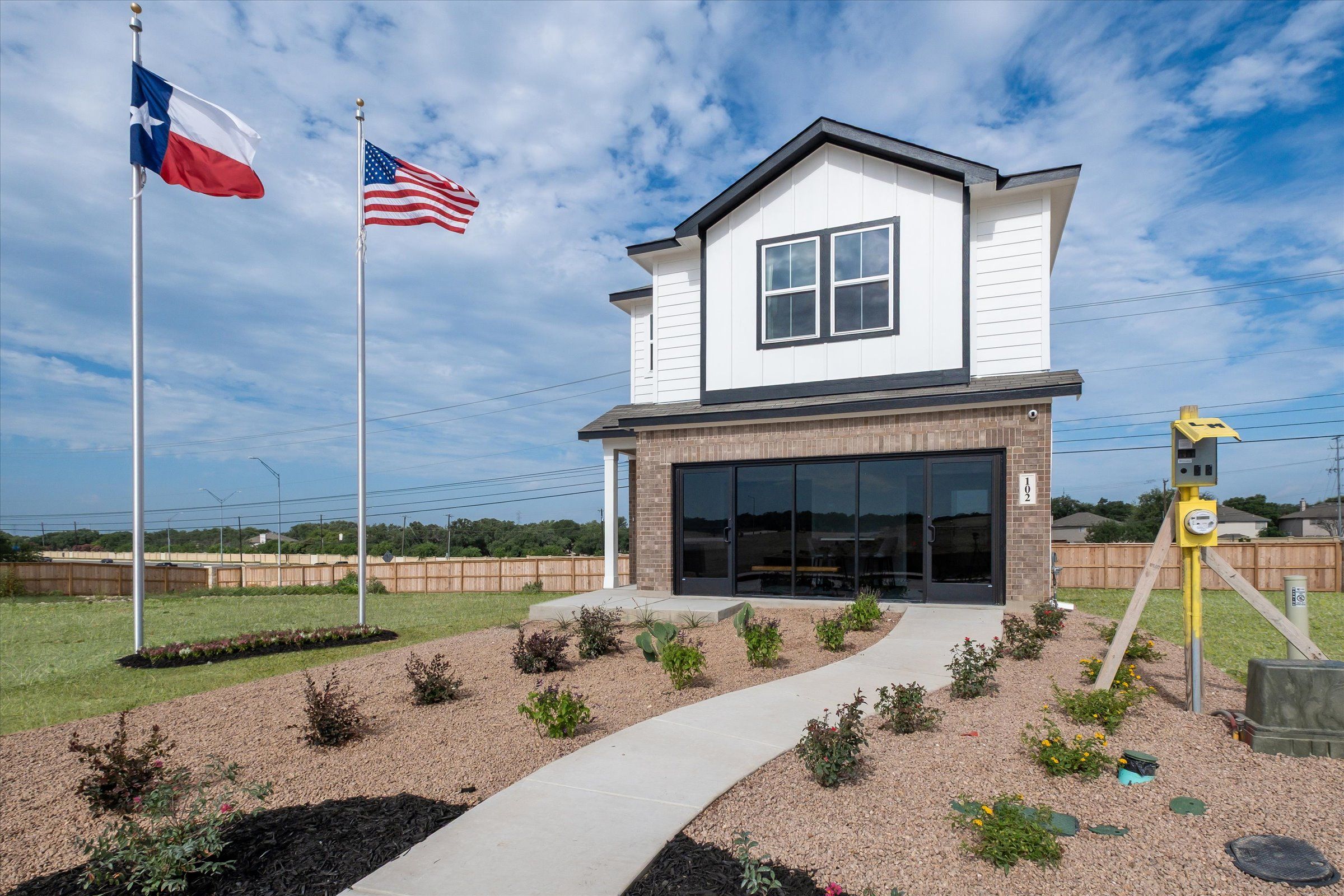 Modern two-story white home with brick base, two-car garage, Texas and US flags, landscaped yard in Meadows at Oak Creek, San Antonio