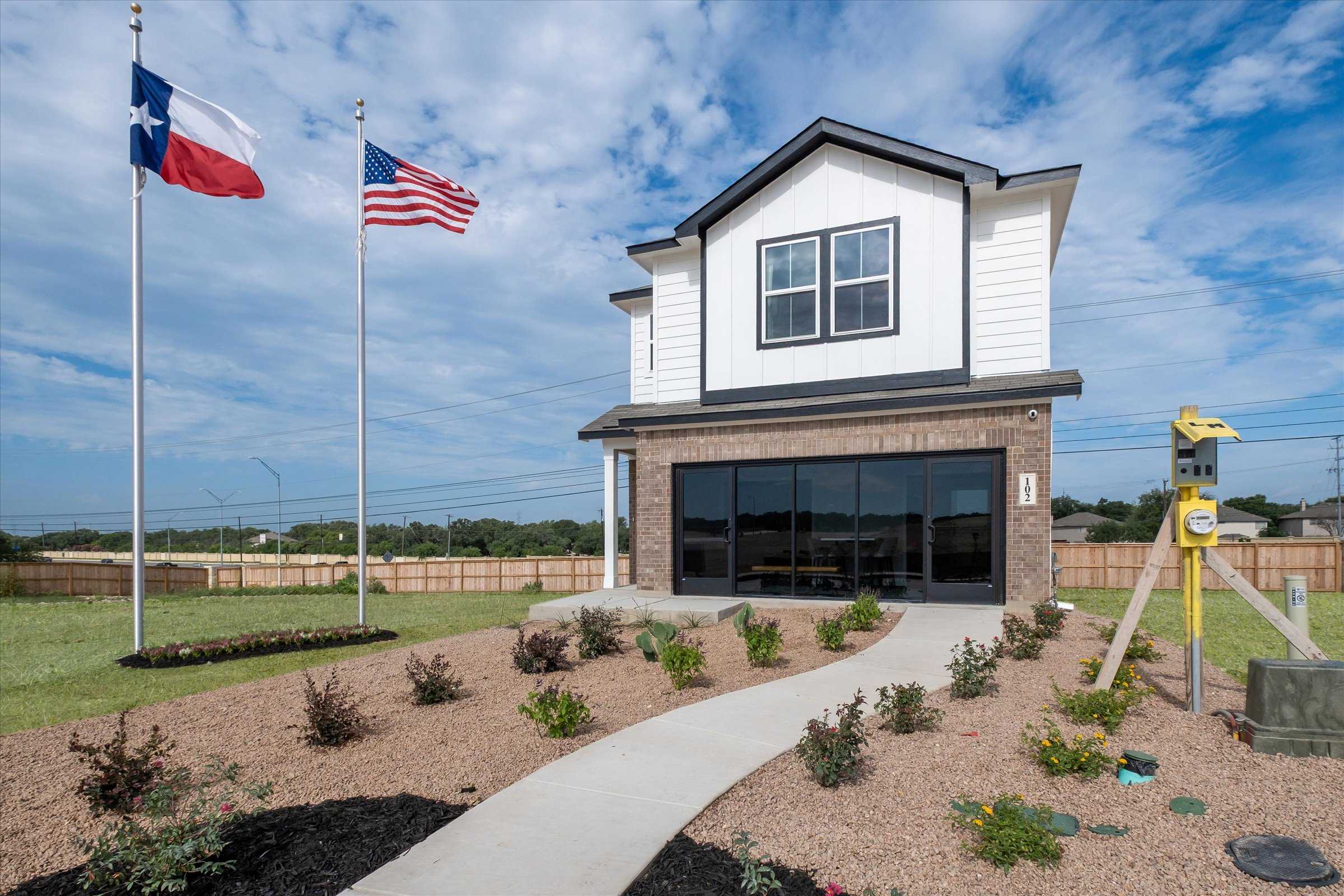 Modern two-story white home with brick base, two-car garage, Texas and US flags, landscaped yard in Meadows at Oak Creek, San Antonio