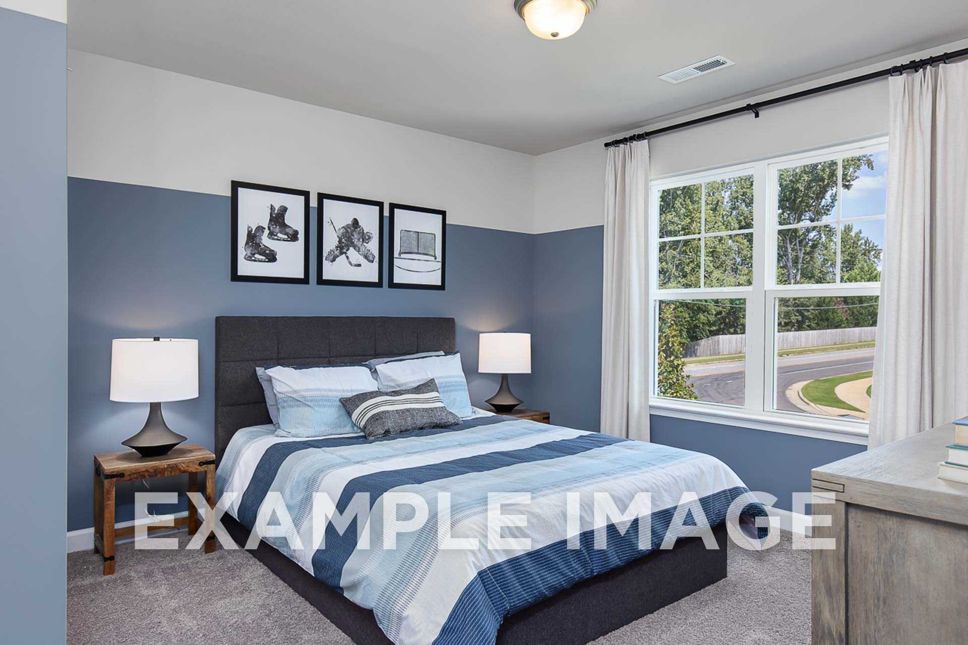 Cozy secondary bedroom in The Ash E home by Davidson Homes with blue accent wall, striped bedding, hockey artwork, and window view of landscaped yard in Angier NC