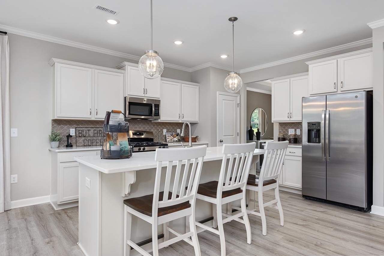 Modern kitchen with white cabinetry, stainless steel appliances, and island seating at Woodland Crossing in Zebulon, NC.
