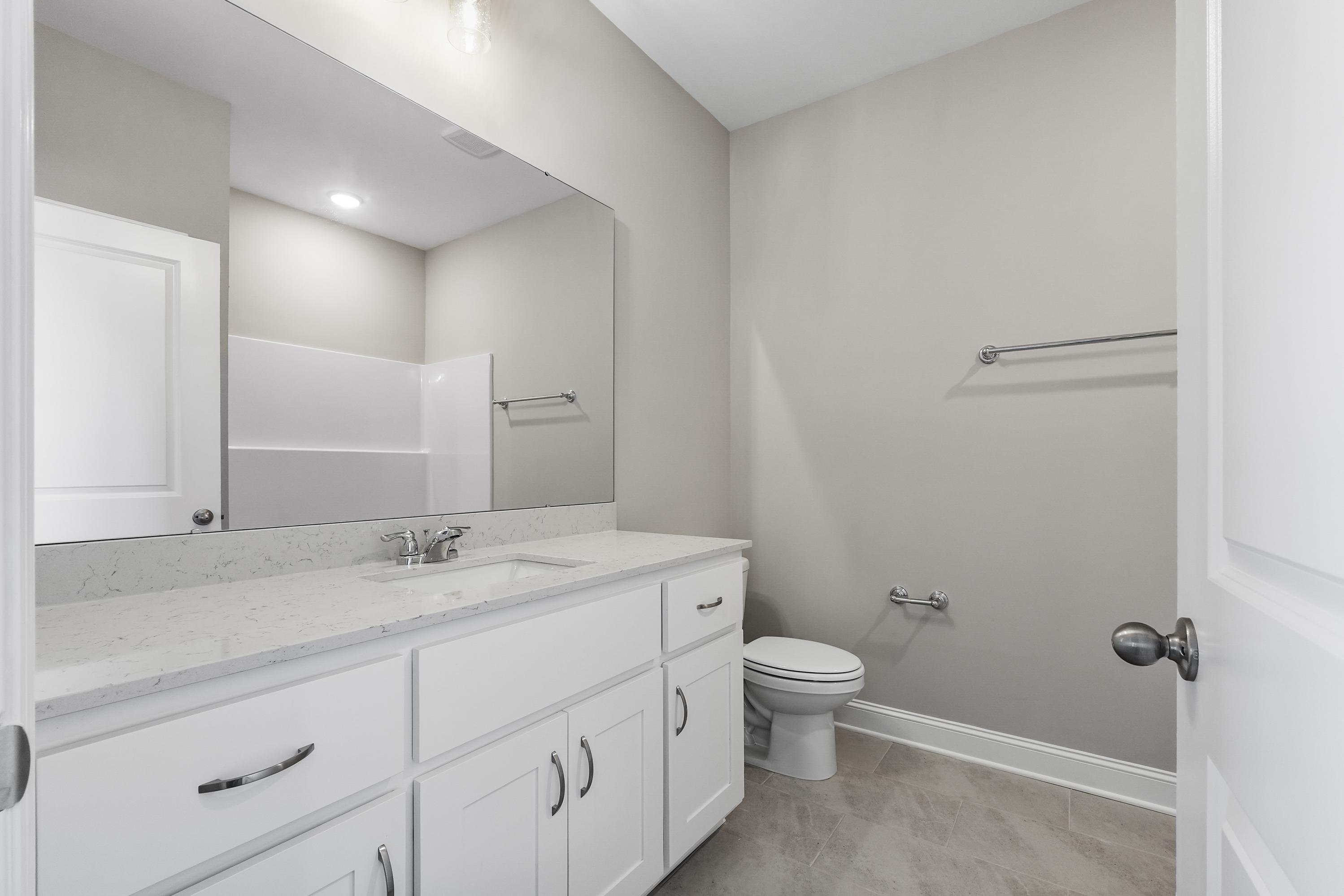 Spacious master bathroom in The Valencia featuring double white vanity, quartz countertop, large mirror, and neutral tones