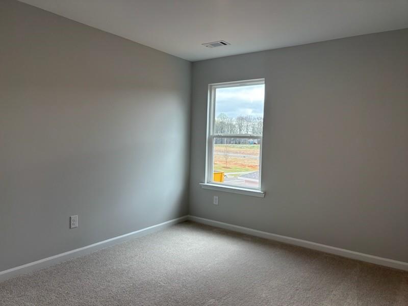 Empty bedroom with gray walls, beige carpet, and window overlooking construction in 5-bedroom Davidson Homes The Hickory B, Winder, Georgia