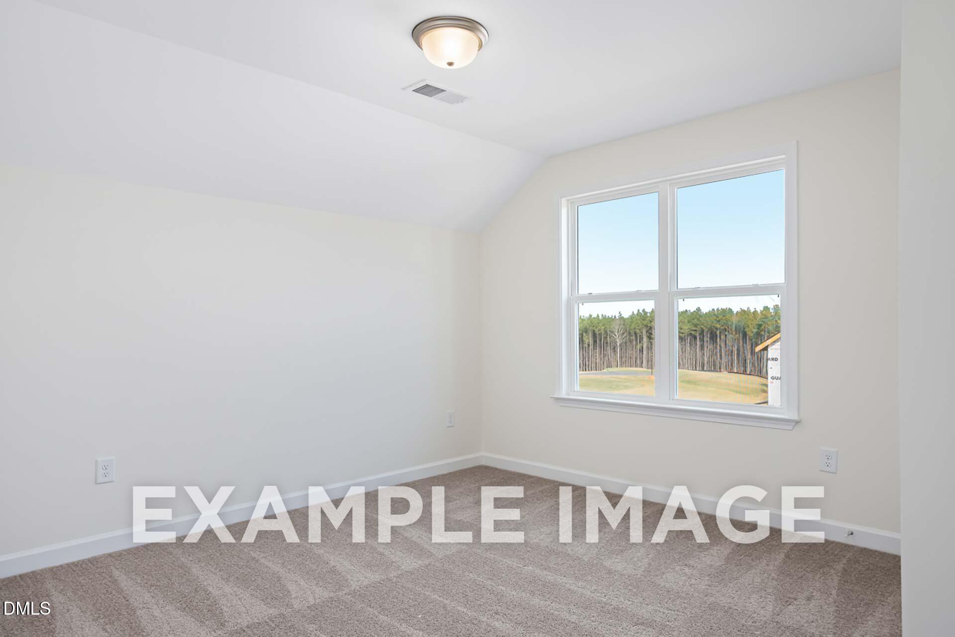 Bright empty bedroom with sloped ceiling, large window overlooking pines in Davidson Homes The Ash B, Zebulon, NC
