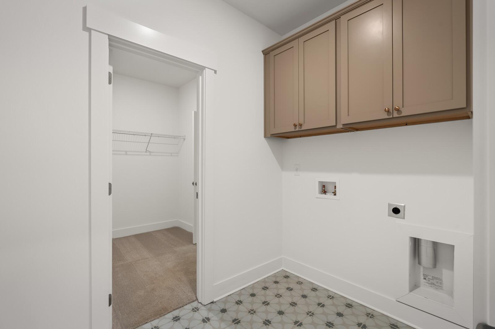 Bright laundry room with beige upper cabinets, washer/dryer hookups, and adjacent closet in Davidson Homes The Ash A, Gallatin, Tennessee