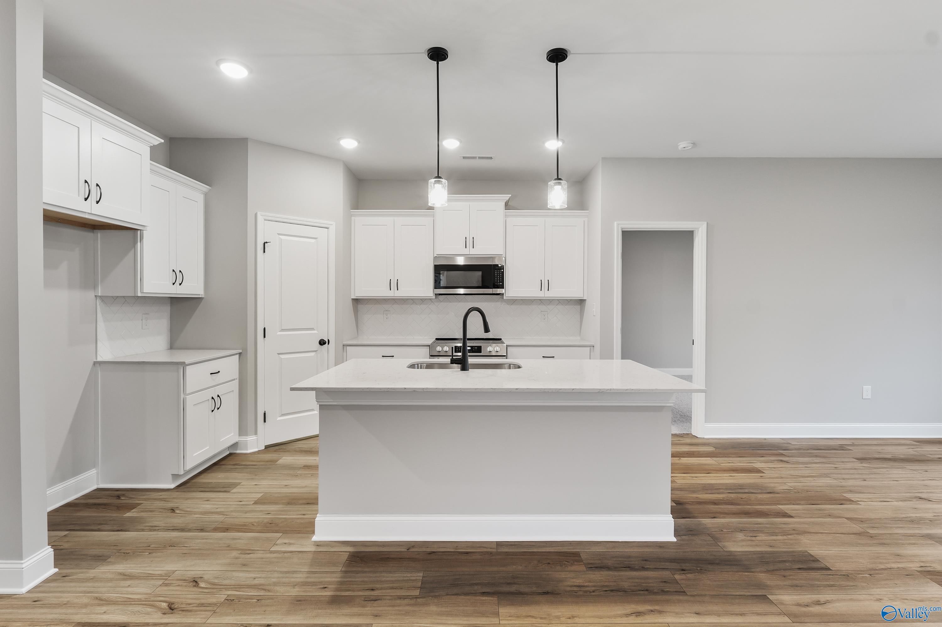 Modern white kitchen with large island, pendant lights, and hardwood floors in The Asheville C by Davidson Homes, Meridianville, Alabama