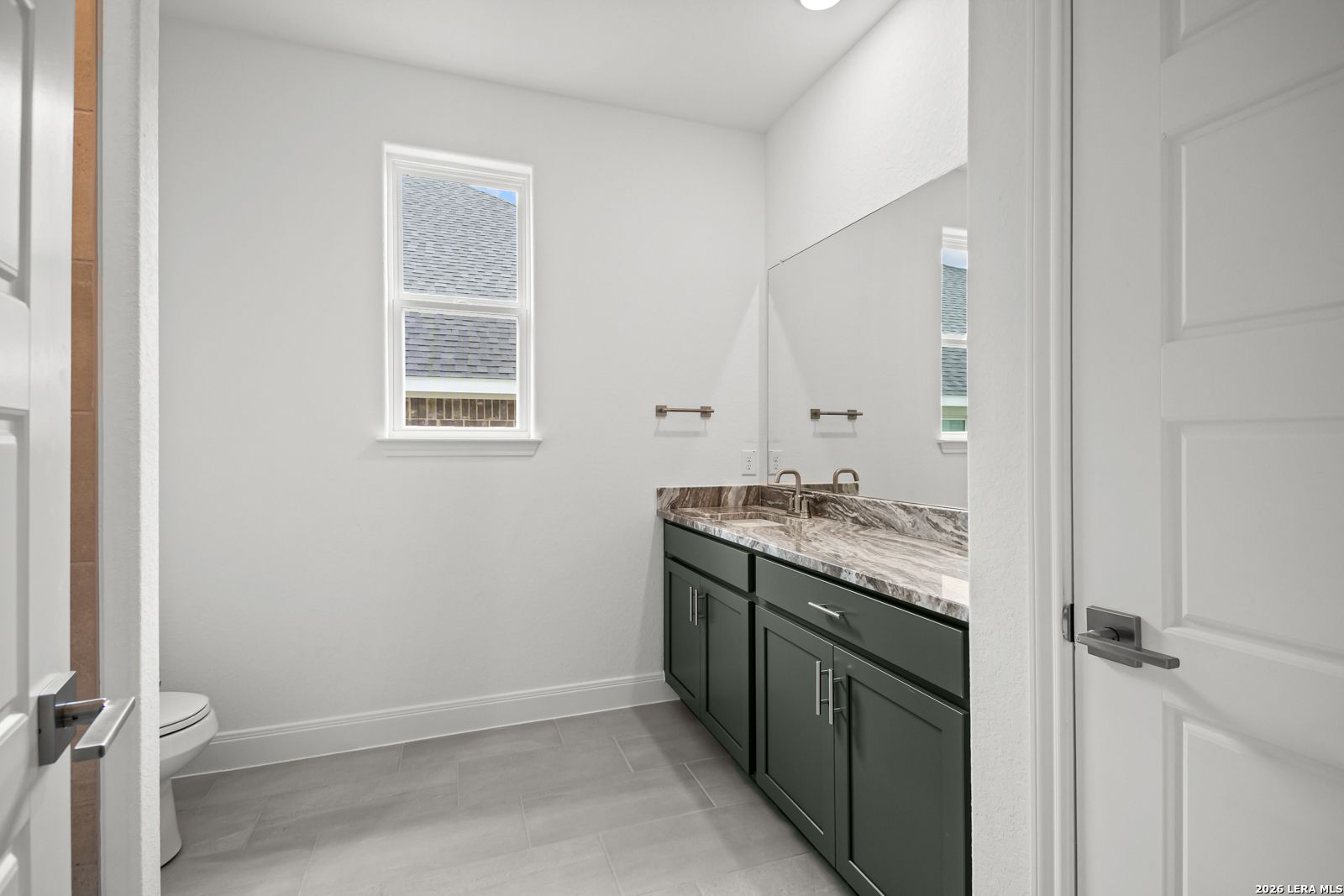 Modern bathroom with dark green vanity, marble-style countertop, and tile flooring in The Lanier G home, Castroville, TX.