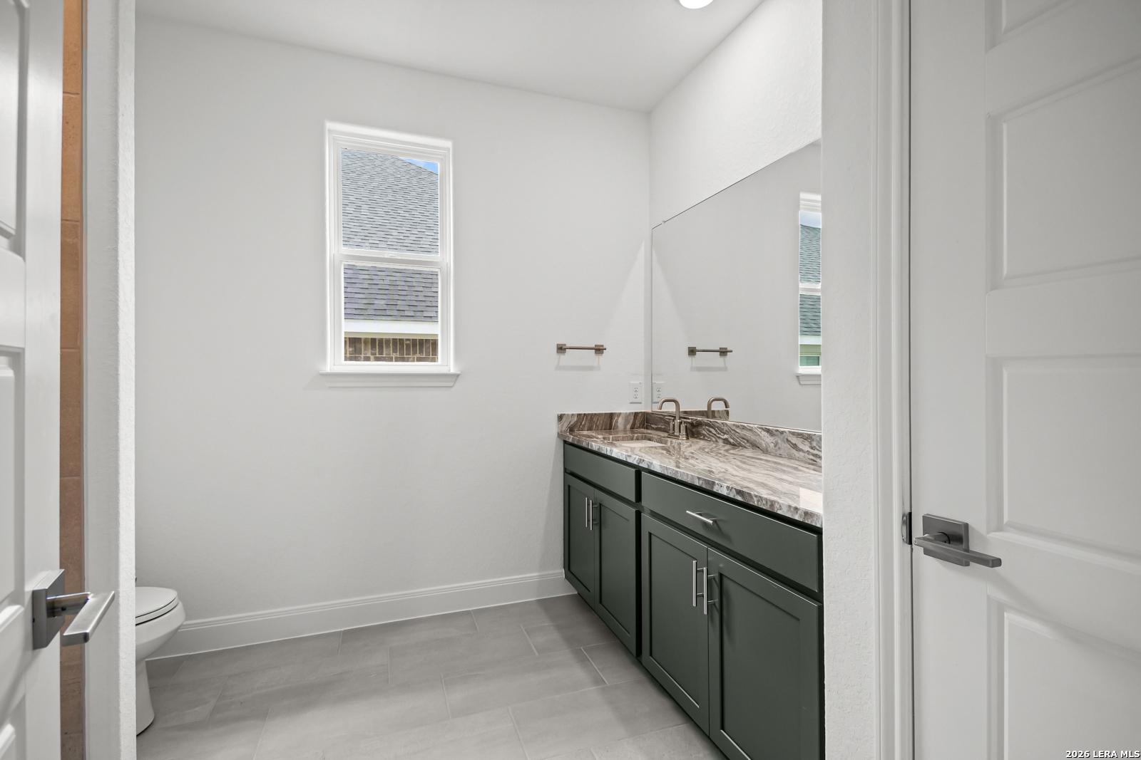 Modern bathroom with dark green vanity, marble-style countertop, and tile flooring in The Lanier G home, Castroville, TX.
