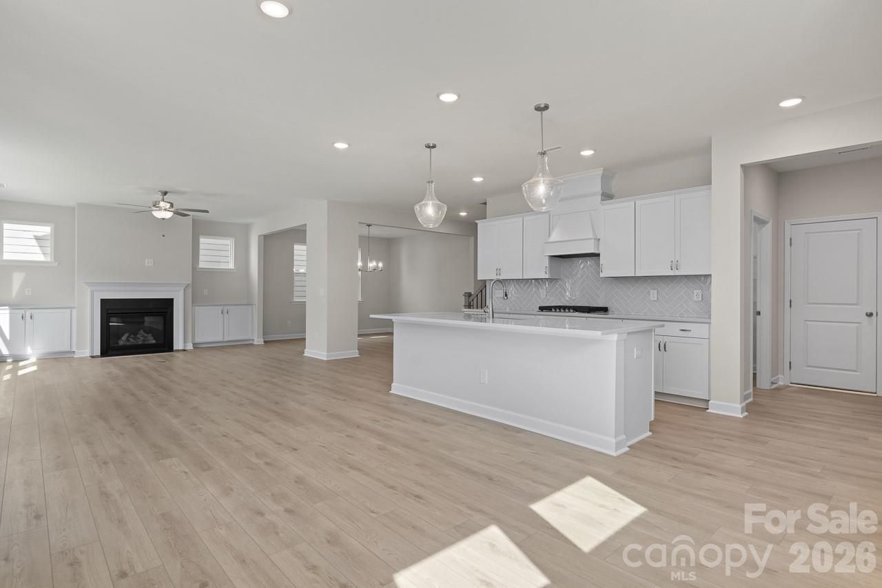 Open-concept great room with white kitchen island, cabinets, herringbone backsplash, gas fireplace, and hardwood floors in Davidson Homes The Beech B, Belmont NC