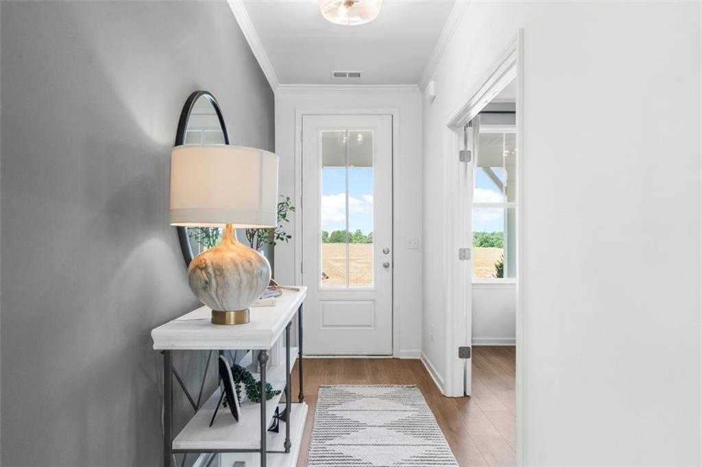 Bright entryway with gray walls, round mirror, gold lamp on console table, and countryside view in Davidson Homes The Hickory B, Hoschton, GA