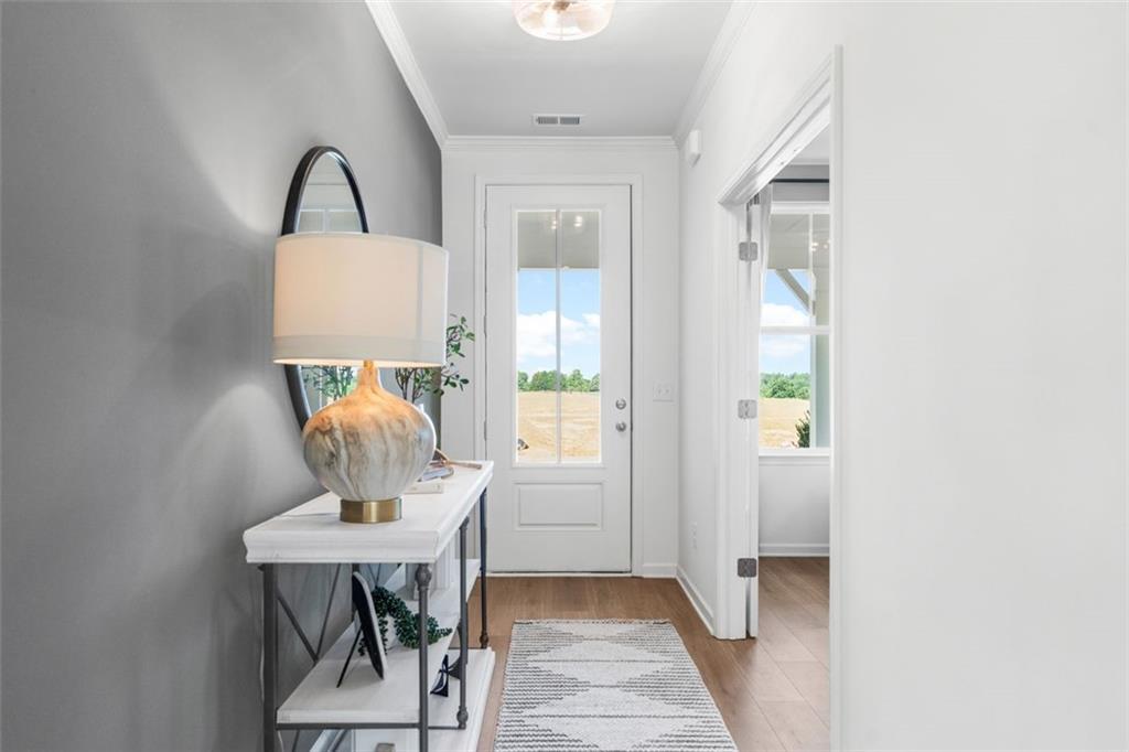 Bright entryway with gray walls, round mirror, gold lamp on console table, and countryside view in Davidson Homes The Hickory B, Hoschton, GA