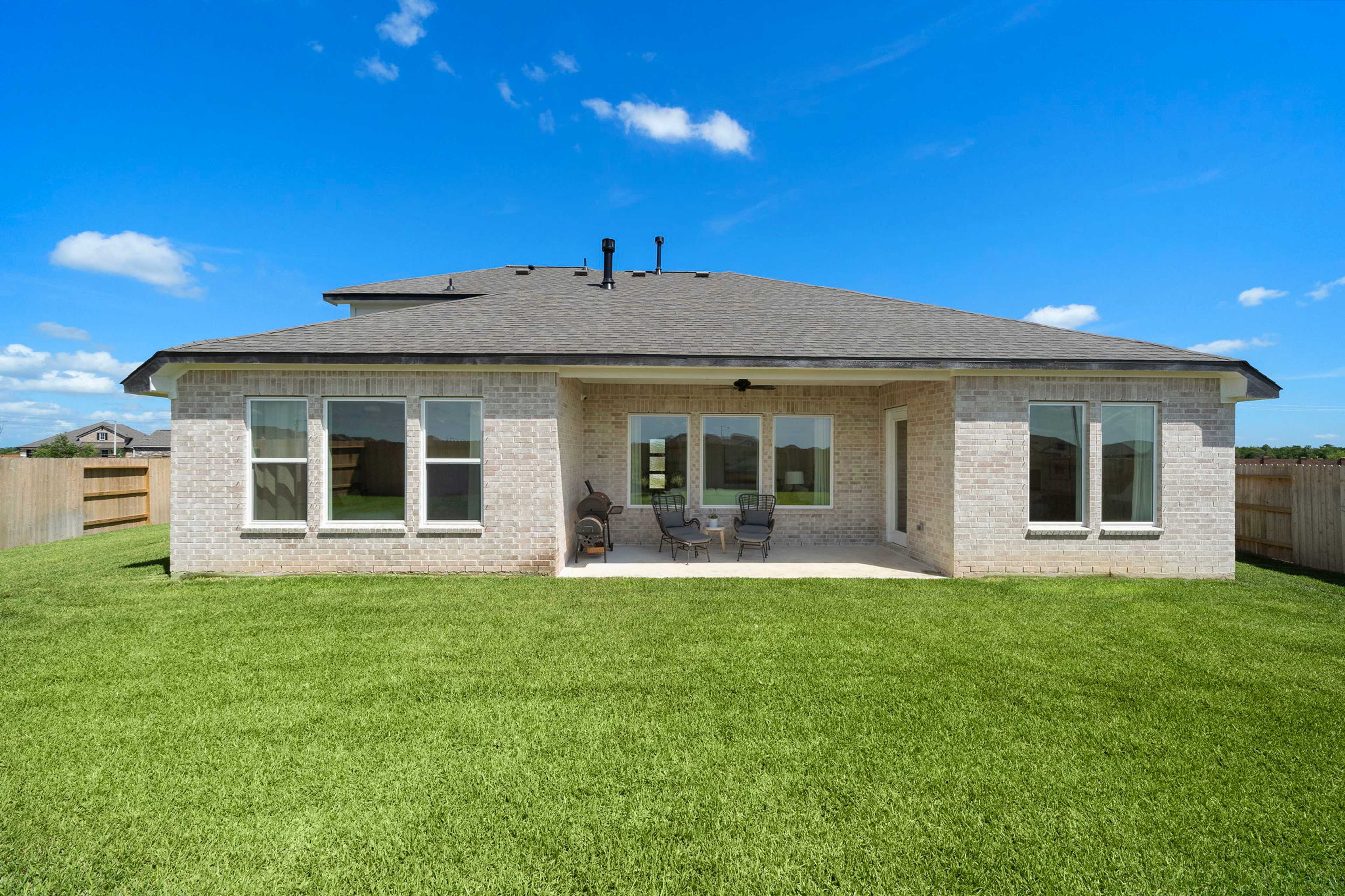 Covered patio with ceiling fans and large windows on modern brick home exterior at Lago Mar in Texas City, Texas by Davidson Homes, lush green lawn