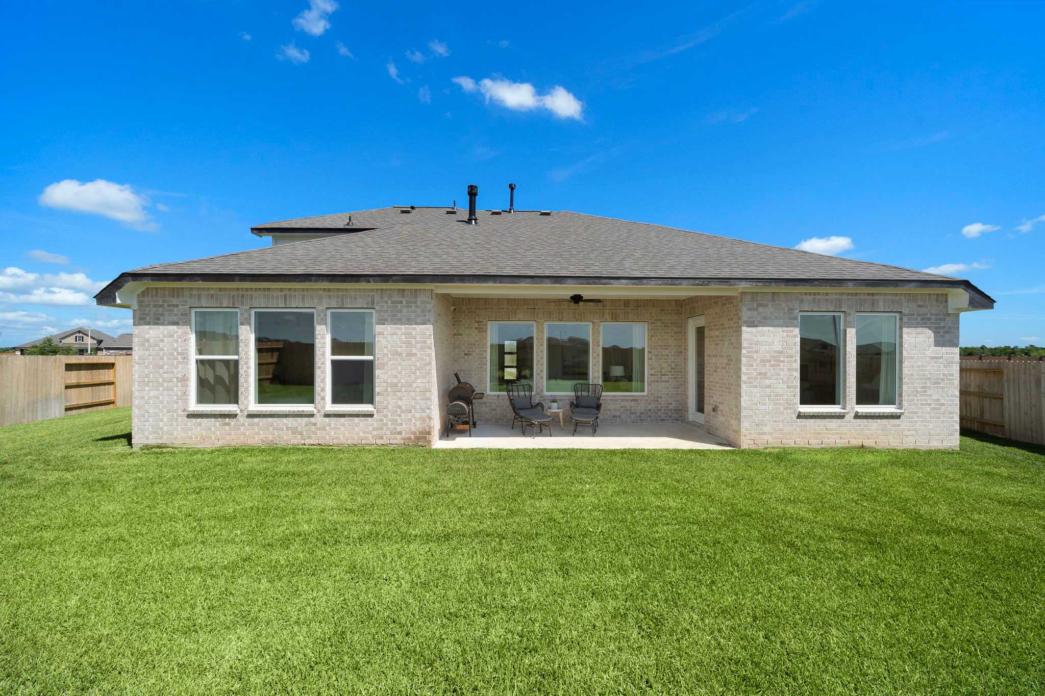Covered patio with ceiling fans and large windows on modern brick home exterior at Lago Mar in Texas City, Texas by Davidson Homes, lush green lawn