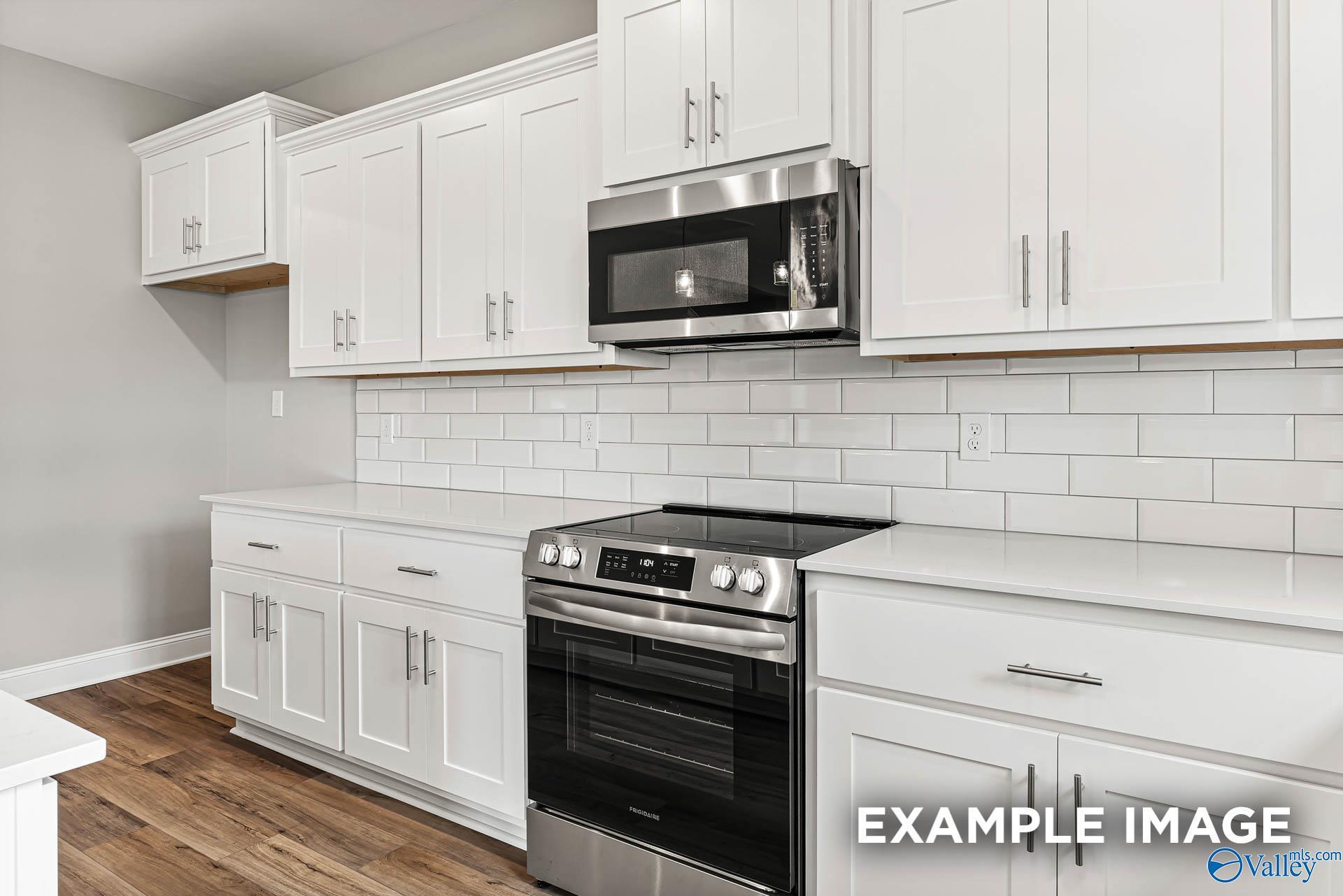 Modern white shaker kitchen featuring stainless steel oven, cooktop, and microwave with subway tile backsplash in Davidson Homes Chelsea B, Toney, AL