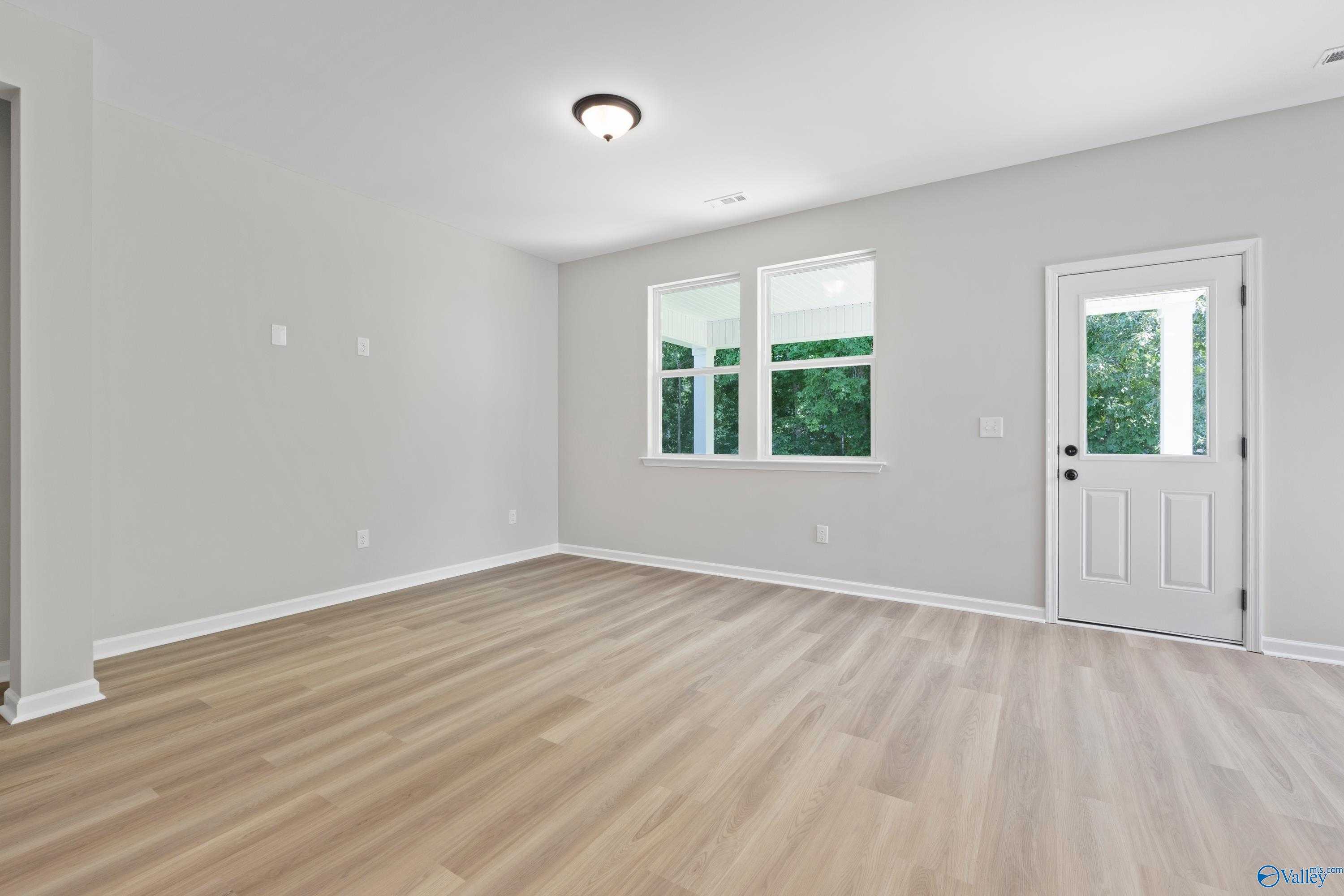 Bright empty bedroom with light gray walls, luxury vinyl plank floors, double windows overlooking greenery in Davidson Homes The Phoenix, Fayetteville TN
