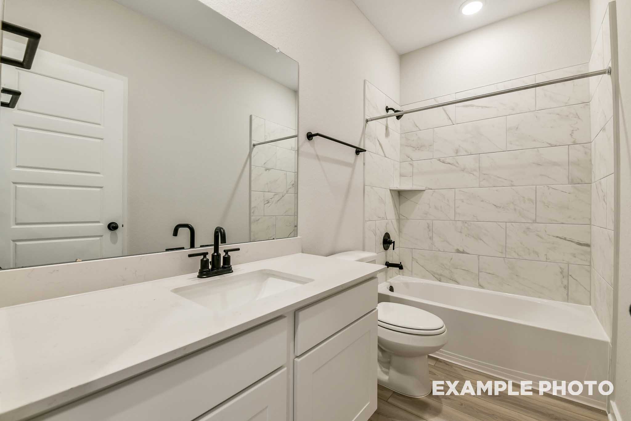 Bright bathroom in The Daphne G by Davidson Homes with white subway tile tub-shower combo, single vanity sink, and black fixtures