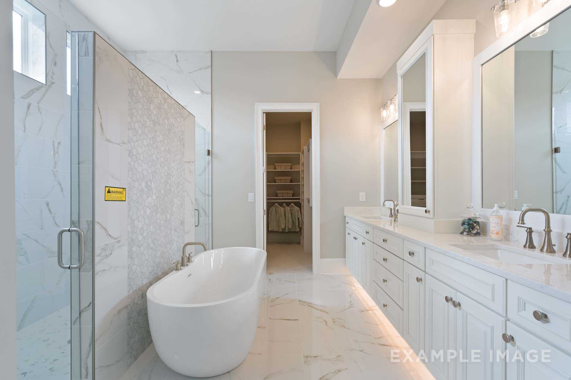 Spacious master bathroom in The Seaside with freestanding white tub, glass shower, double vanity, and walk-in closet
