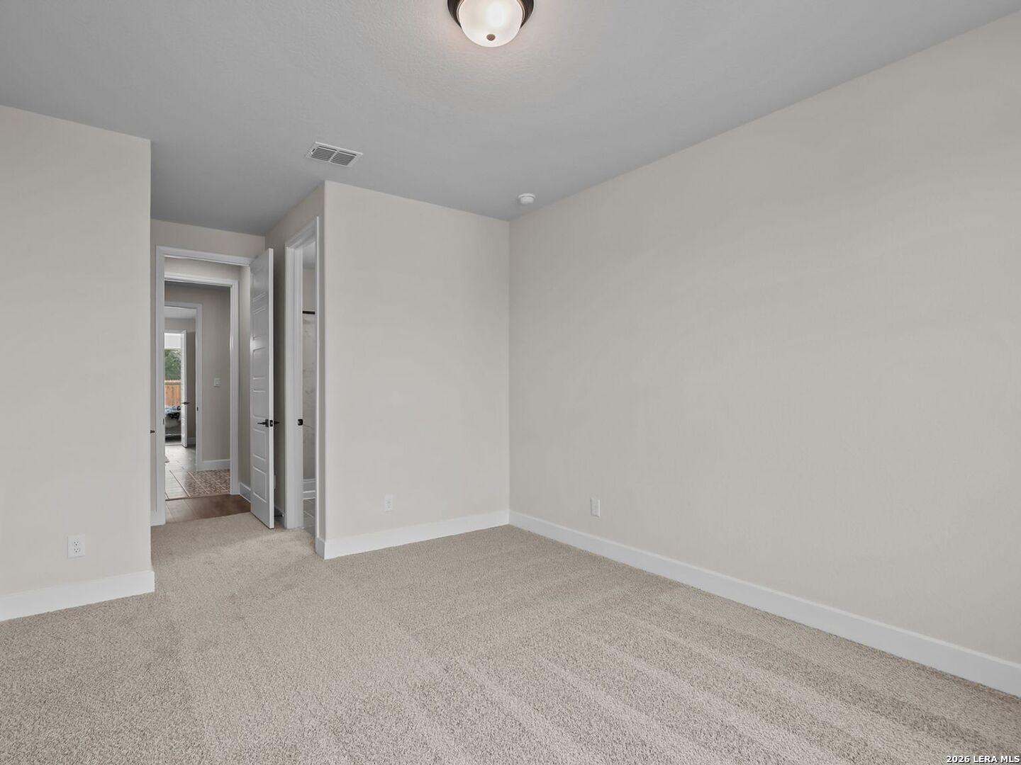 Spacious carpeted bedroom with neutral walls in The Belmont H floor plan at Potranco Oaks, Castroville, Texas.