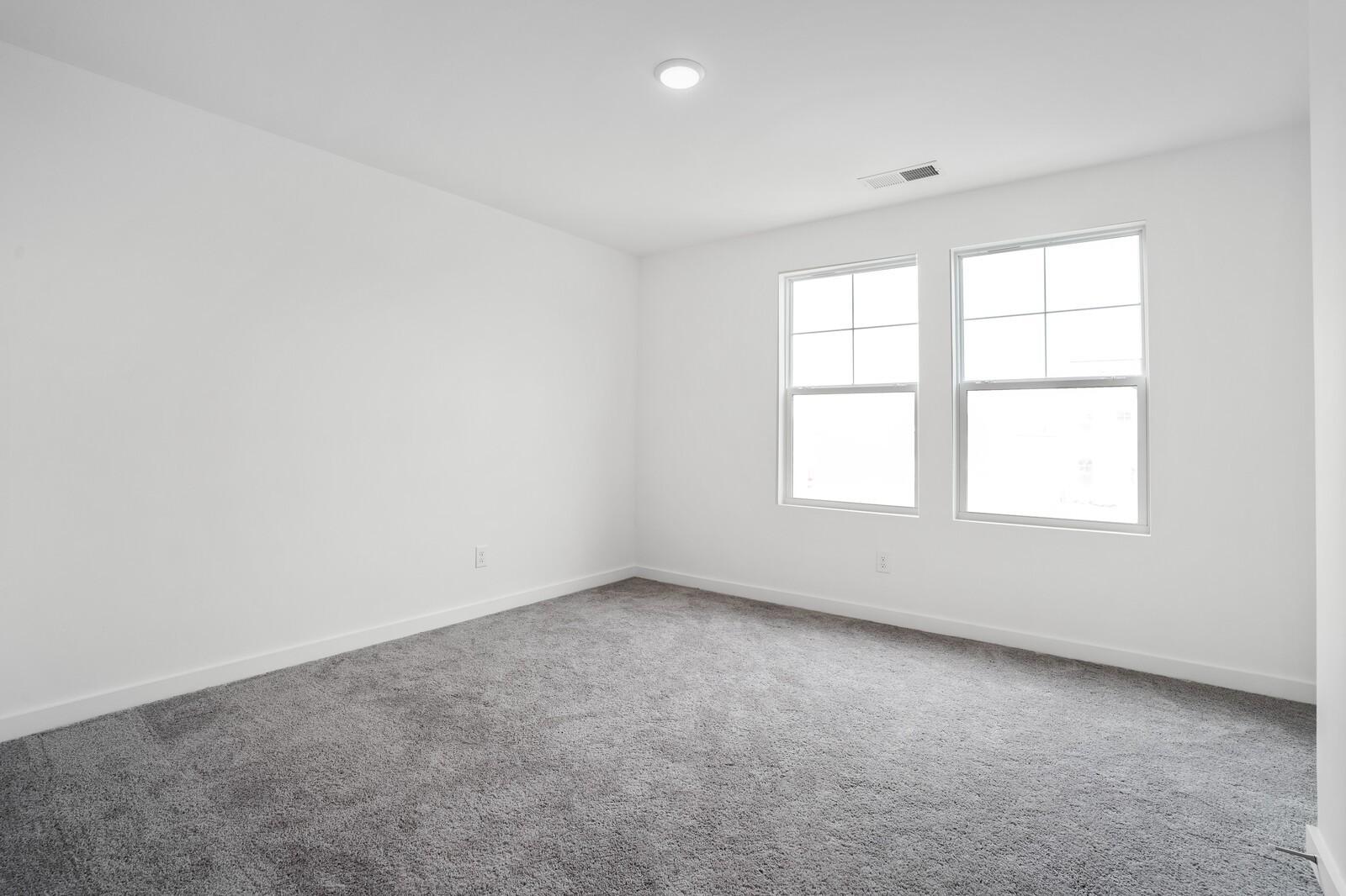 Bright secondary bedroom featuring white walls, large windows, and plush gray carpet in Davidson Homes The Logan C, Calista Farms, White House, TN