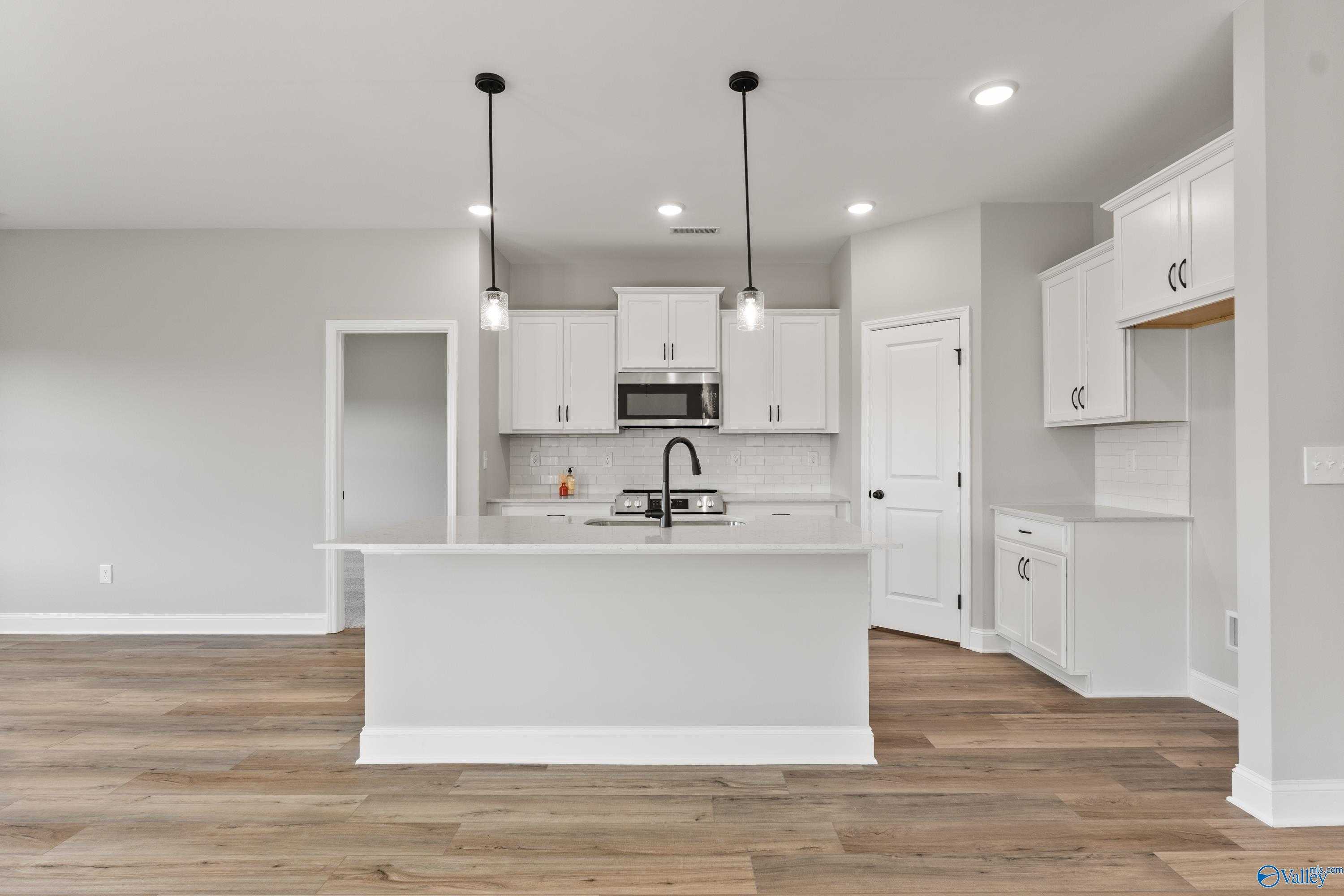 Modern white kitchen island with stainless appliances, pendant lights, and hardwood floors in Davidson Homes The Franklin B, Hazel Green, AL