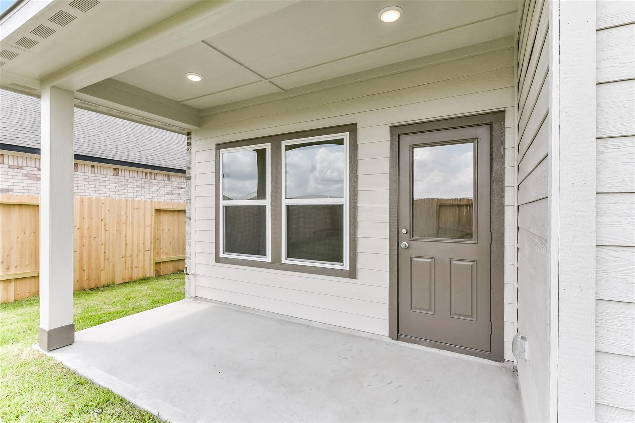 Covered back patio with recessed lights, glass door, and windows overlooking grassy yard in Davidson Homes The Costa B, Dayton, Texas