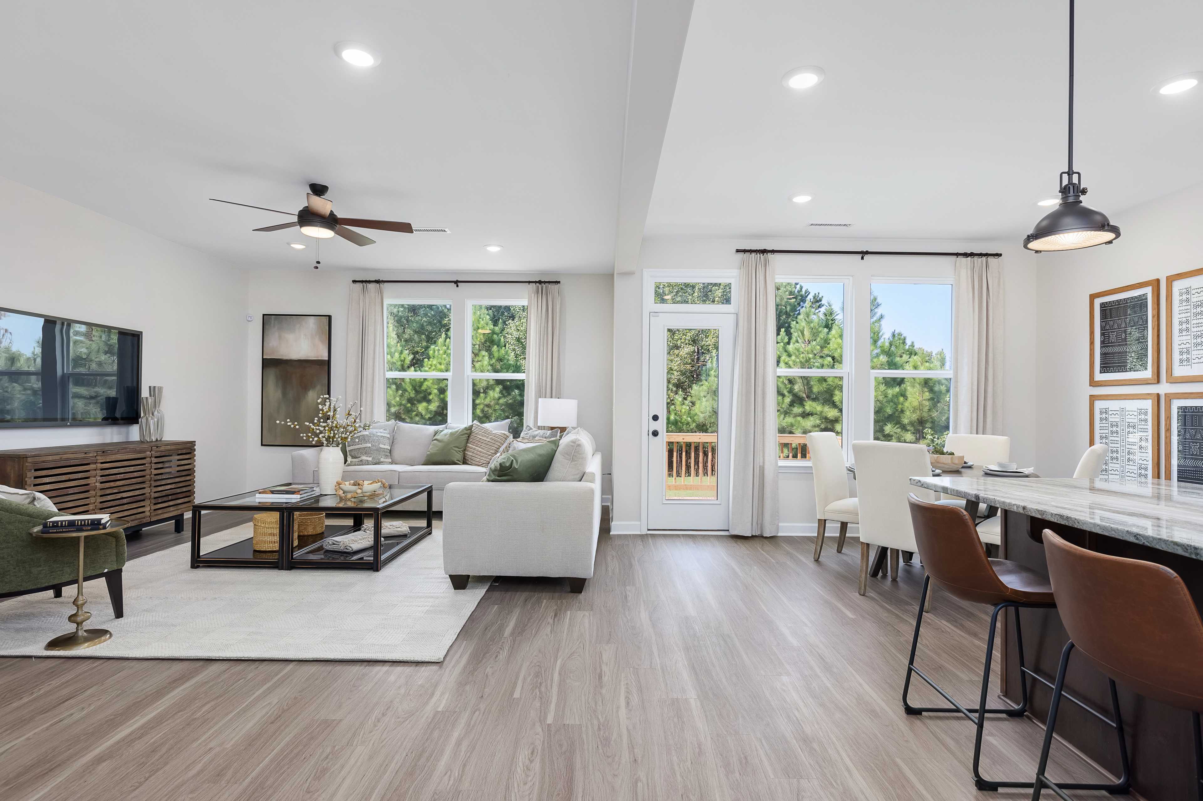 Open-concept living room and kitchen at Woodland Crossing in Zebulon NC by Davidson Homes with hardwood floors, white sofas, and large windows