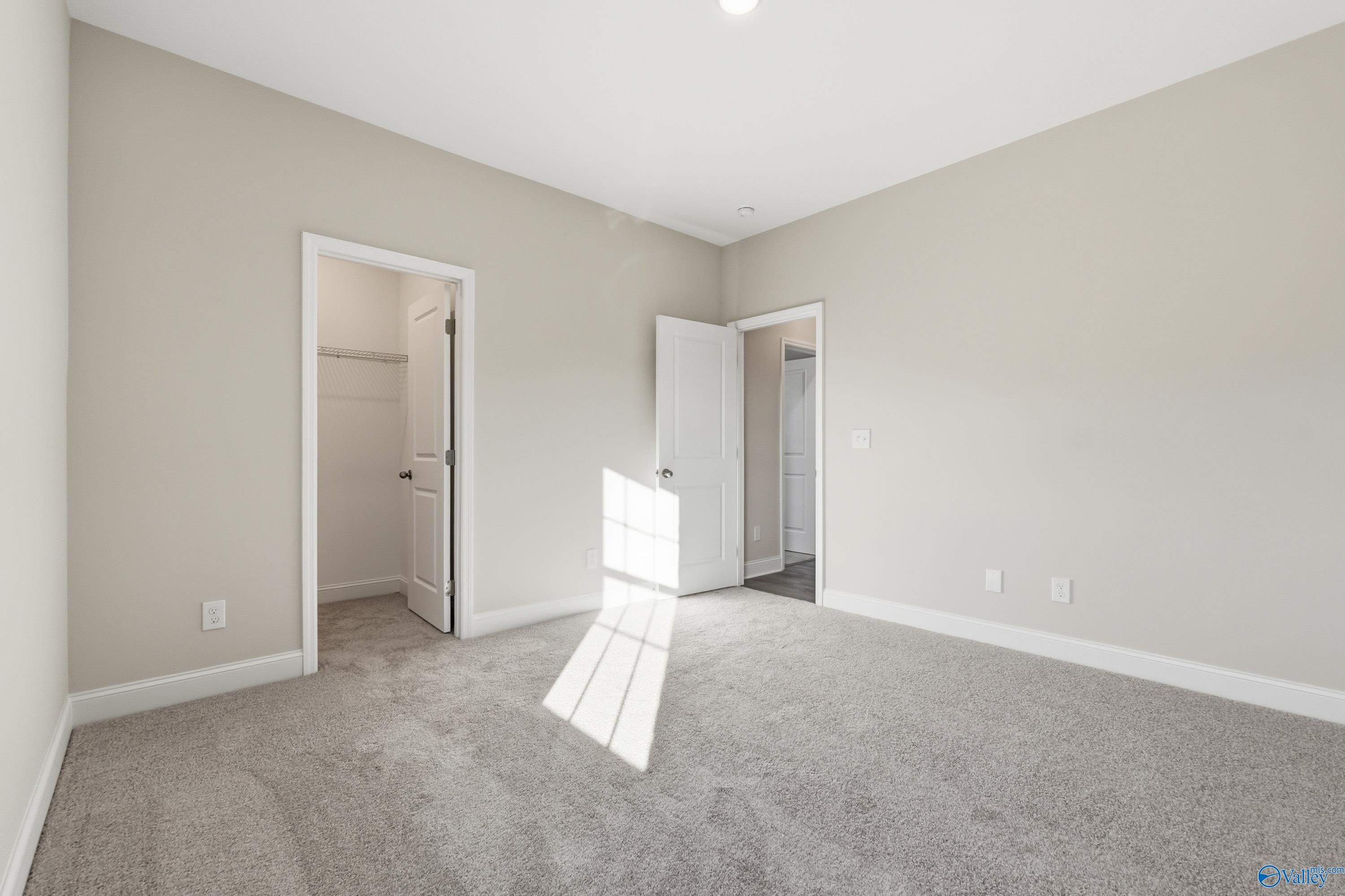 Spacious empty bedroom with beige walls, carpet floor, closet door and adjacent bath entry in Davidson Homes The Montgomery B, Toney, AL