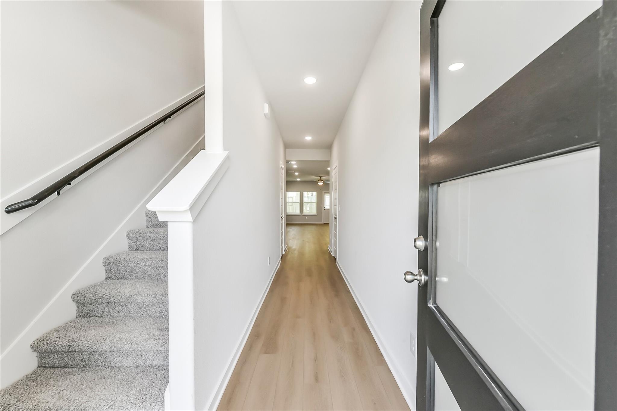 Bright hallway with carpeted staircase, hardwood floors and modern glass-front door in 5-bedroom The Brazos E home, Windmill Estates, Magnolia, Texas
