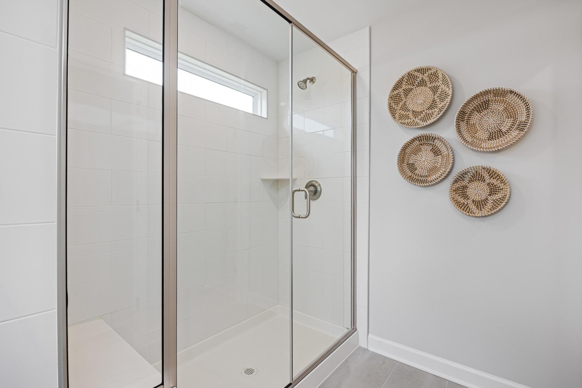 Walk-in glass shower in a modern bathroom at Gregory Village in Lillington, NC, featuring decorative wall baskets.